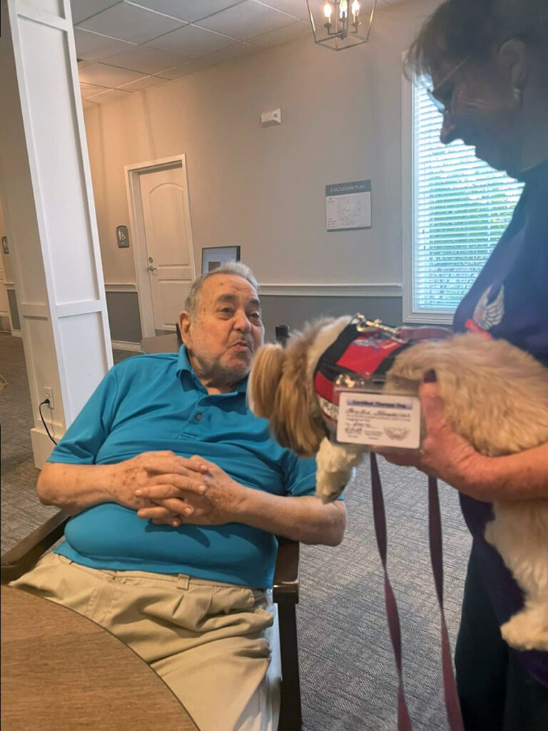A volunteer brings a therapy dog to The Neighborhood, bringing smiles to a memory care resident's face.